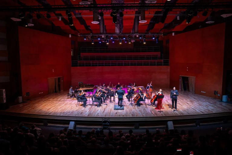 Orquesta filarmónica tocando en concierto en vivo con iluminación escénica